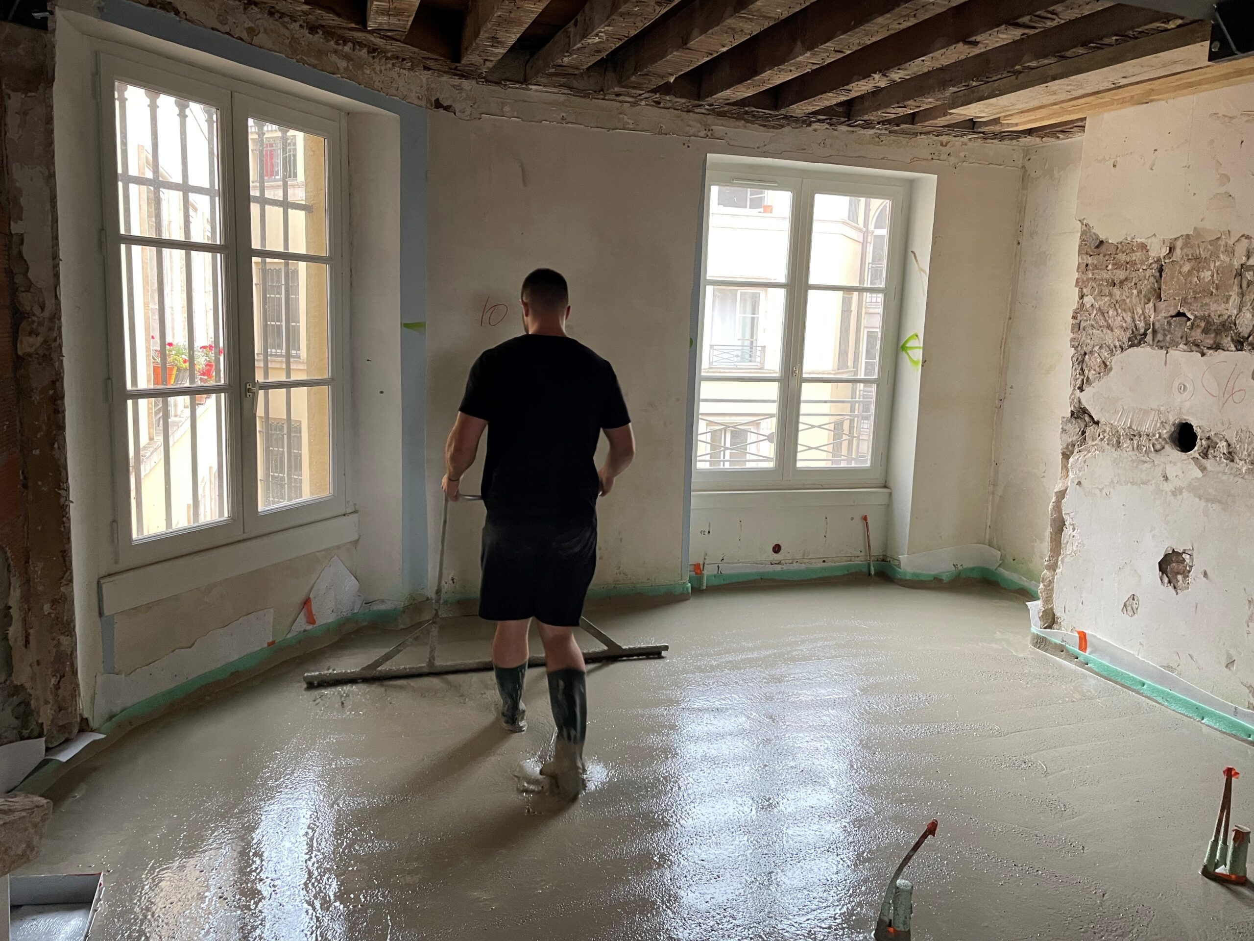 Chapiste égalisant une chape liquide fraîche à la barre de dressage dans un appartement en rénovation